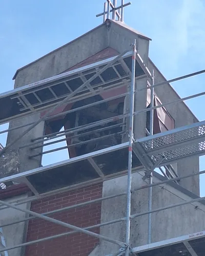 Rusztowanie ramowe wokół betonowej dzwonnicy z ceglaną podstawą