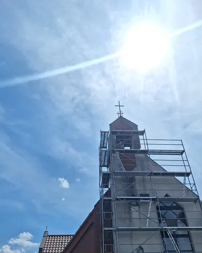 Rusztowanie ramowe na całej wysokości wieży kościoła, słońce nad krzyżem