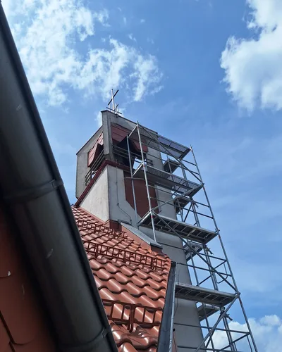 Rusztowanie na wieży kościoła widziane ponad krawędzią ceramicznego dachu