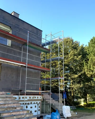 Rusztowanie ramowe przy wejściu do budynku, przed nim schody i materiał budowlany