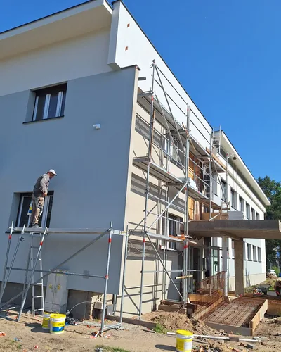 Pracownik odwrócony plecami pracuje przy ścianie, stojąc na pomoście niskiego rusztowania